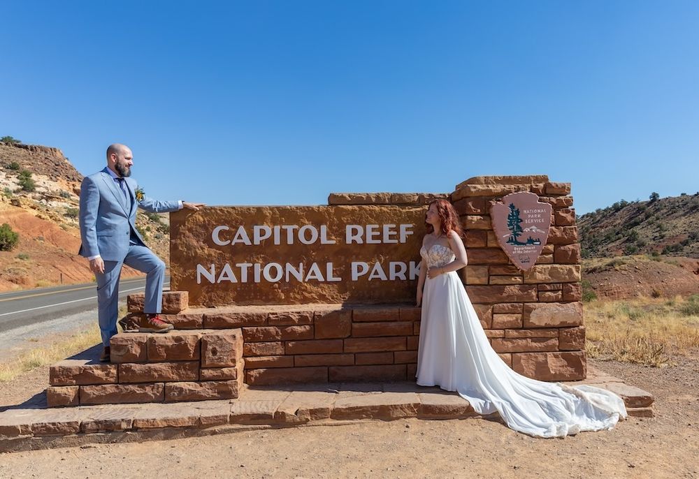 A couple poses at various scenic spots in Capitol Reef National Park with red rock formations and park signs in view.