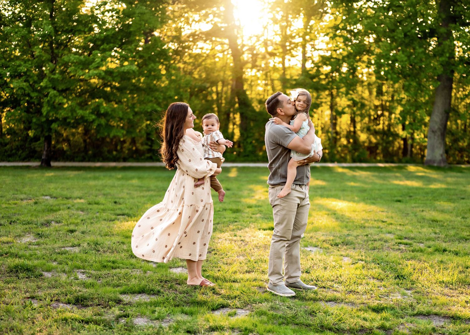 Family enjoying a golden sunset together in a grassy park with sunlight streaming through trees.