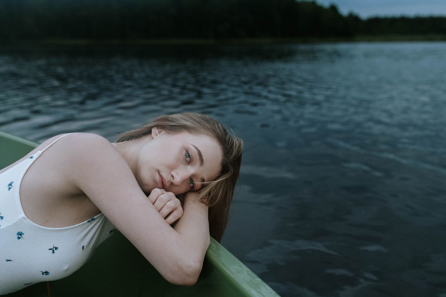 Person floating peacefully in dark water while wearing a white sleeveless top.