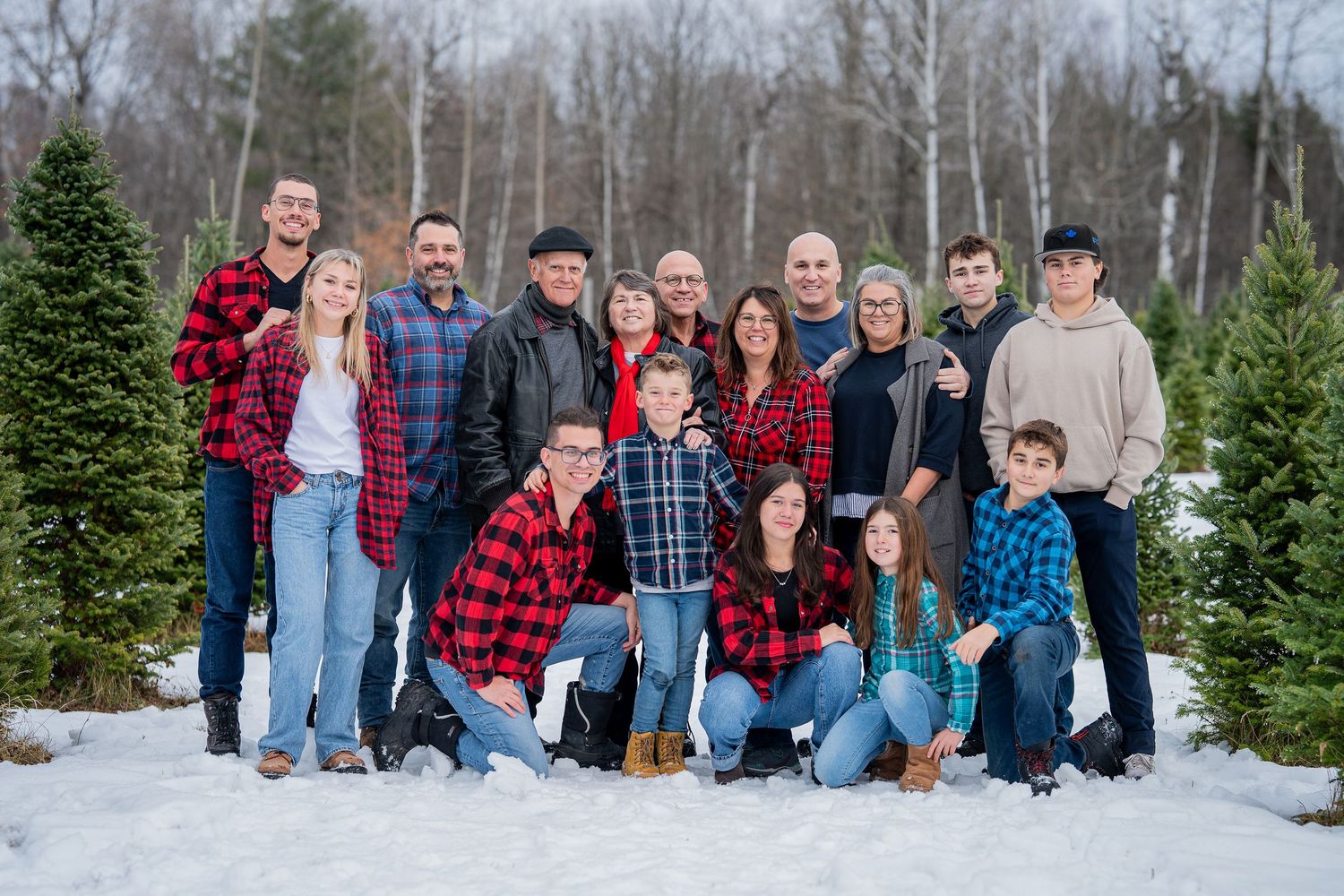 A group gathers outdoors at a snowy Christmas tree farm on a winter day wearing cozy plaid and winter attire.
