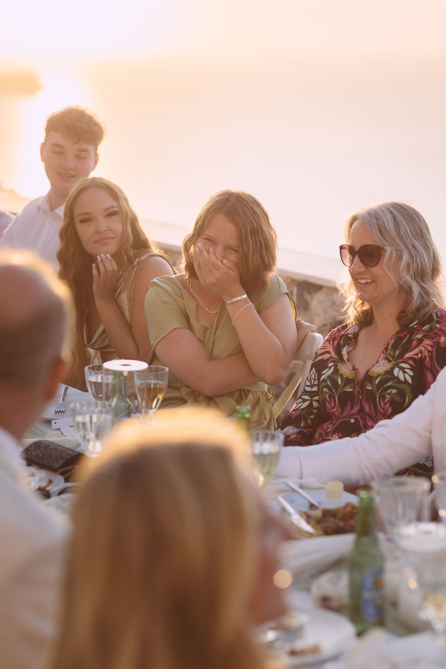 Guests laughing at a table at a Santorini destination wedding at sunset.