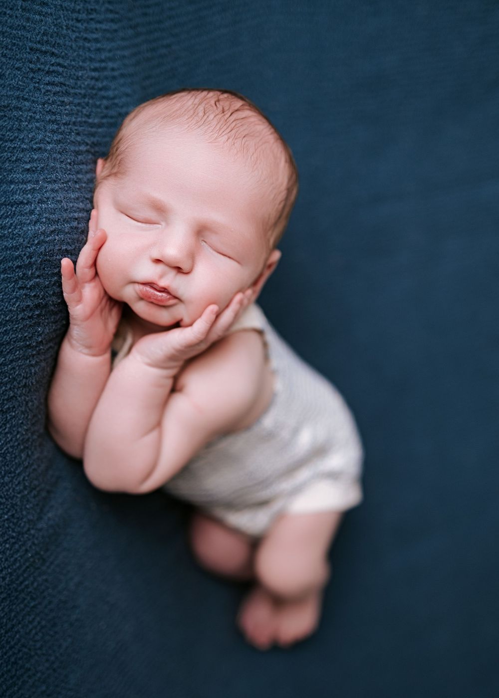 Sleeping newborn in white diaper against dark blue textured background.