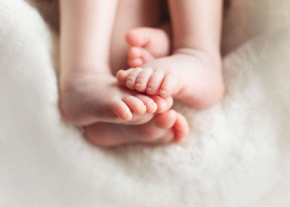 Close-up of tiny newborn feet and toes against soft white fabric.