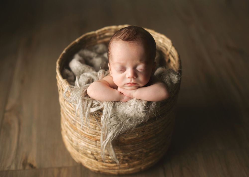Sleeping newborn nestled in a rustic woven basket with textured fabric.
