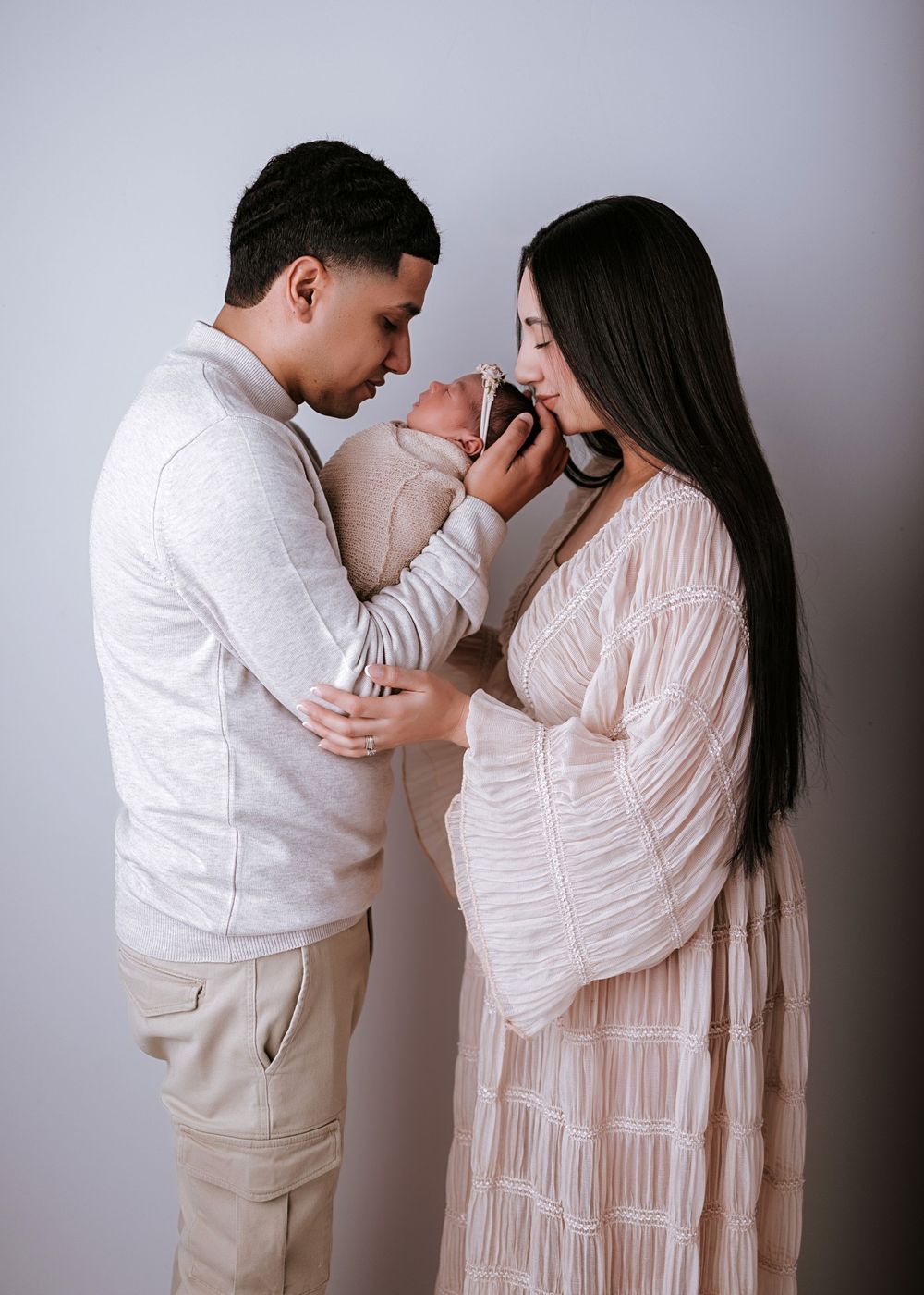 Family photo series in white outfits showing tender moments against grey backdrop.
