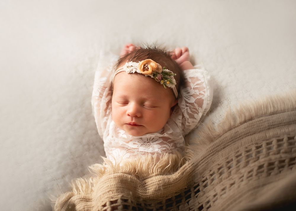 Serene newborn resting on textured fabric with golden headpiece.