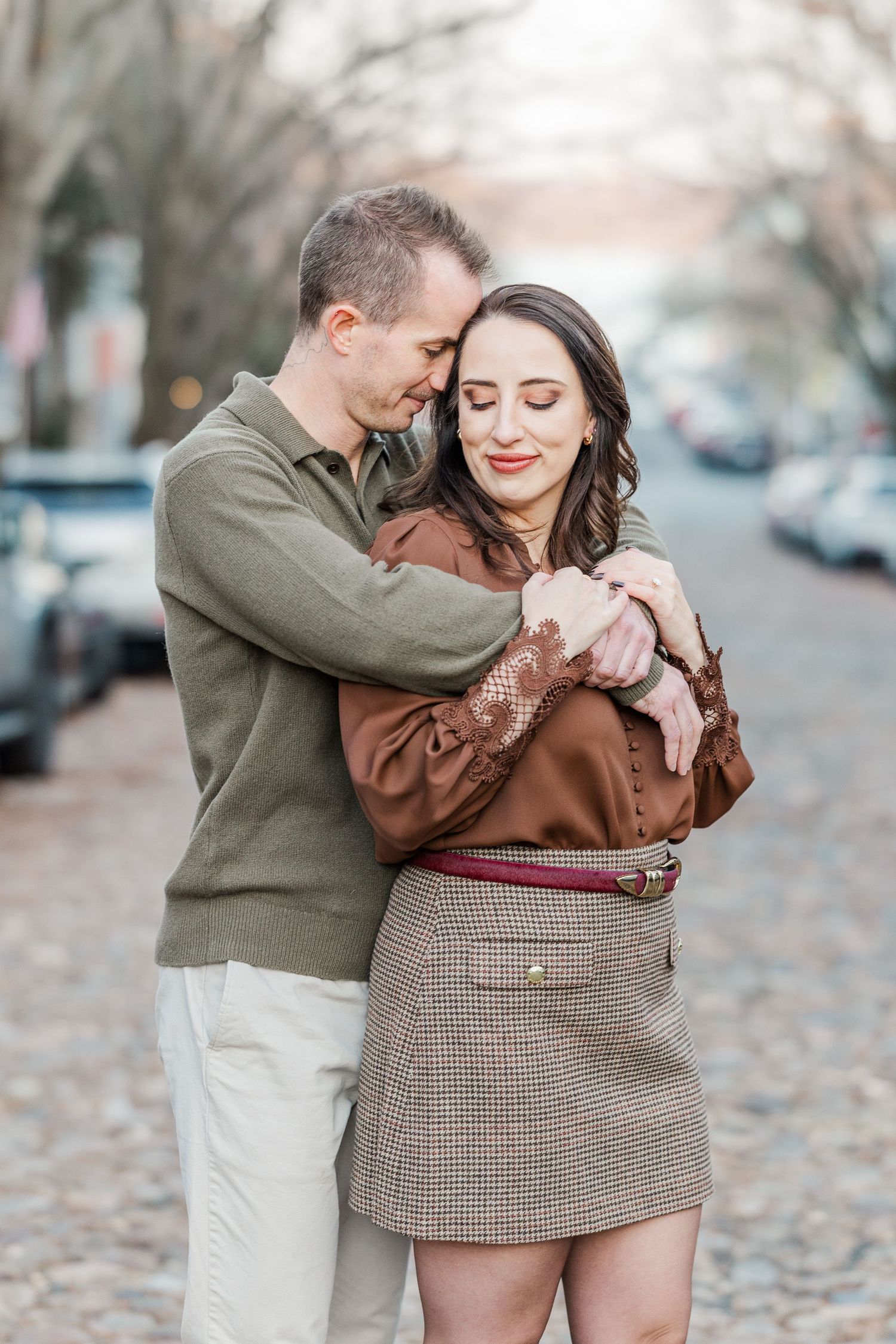 A couple embraces tenderly on a city street with autumn leaves scattered around them.