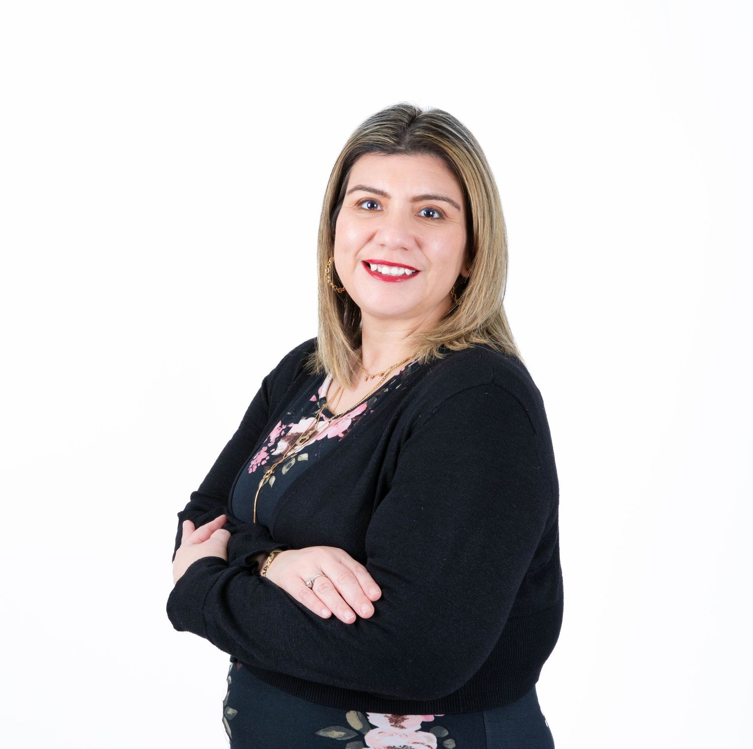 Professional portrait of someone in a black cardigan and floral top standing against a white background with arms crossed.