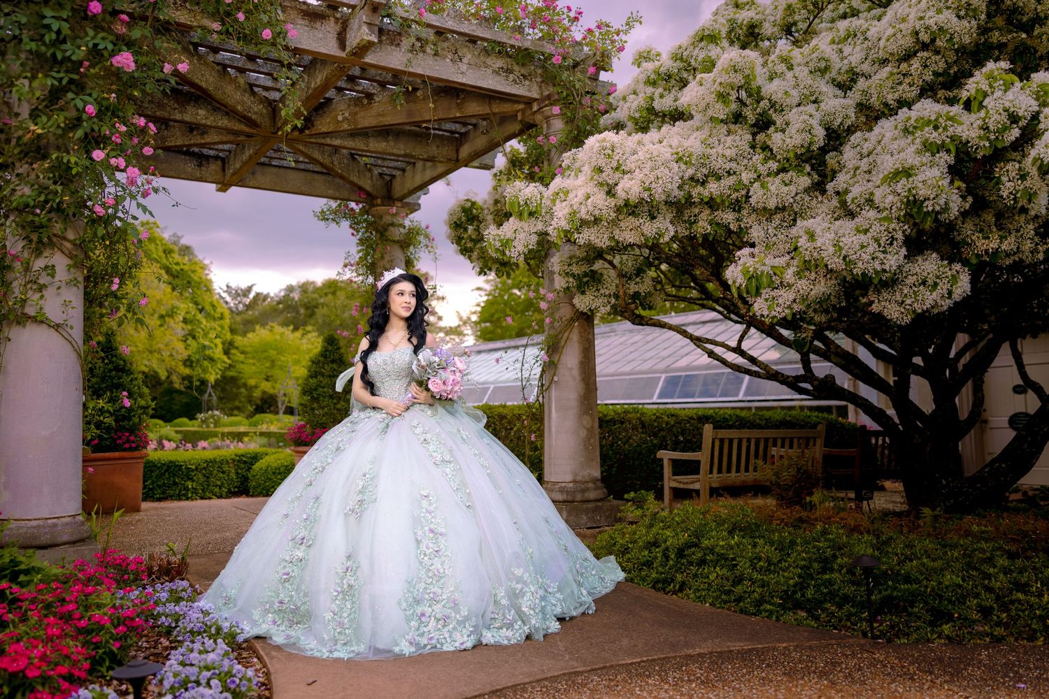 Bride in elegant white ball gown poses in a garden setting with blooming cherry blossoms and spring flowers.
