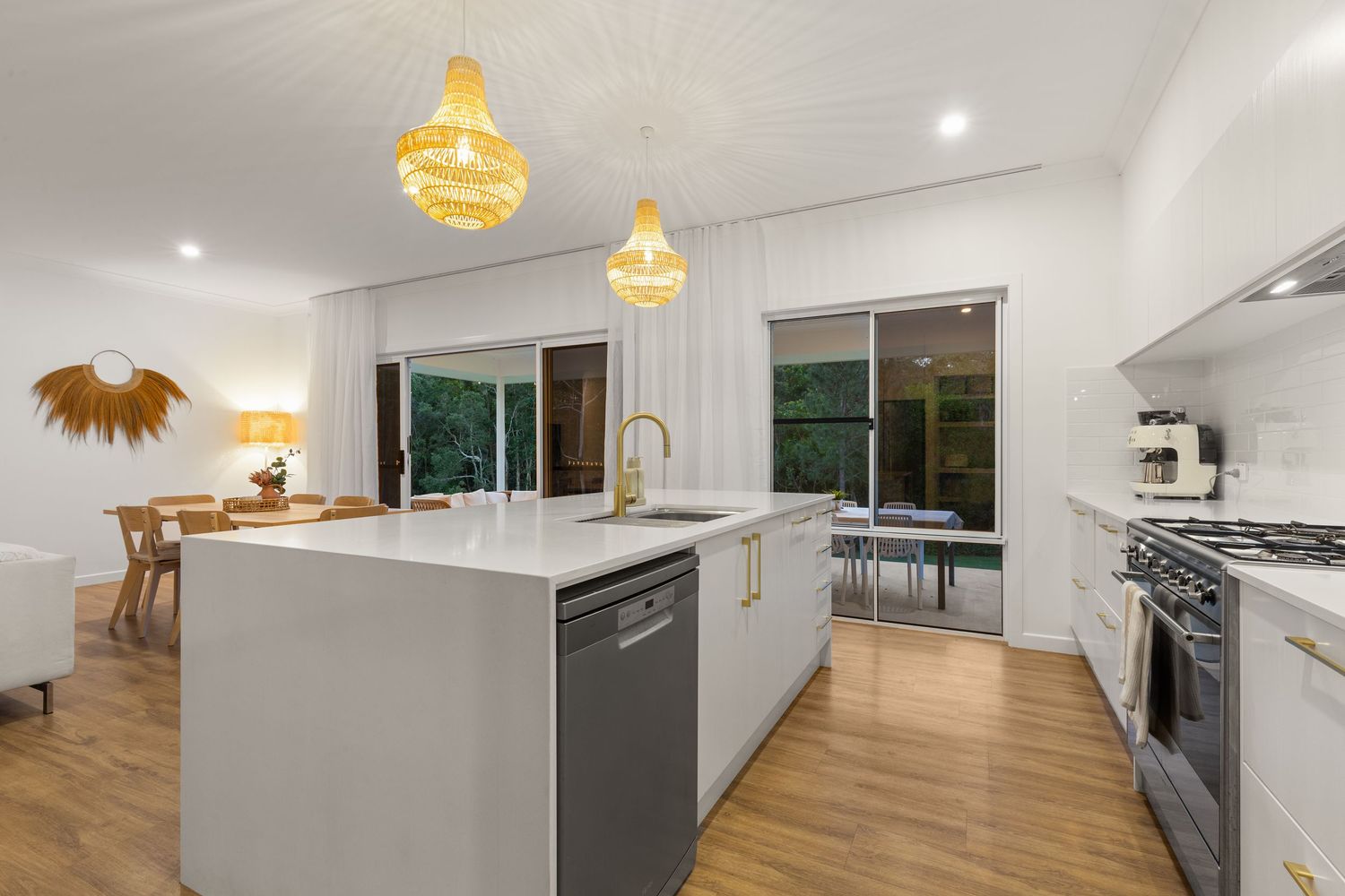 Stylish kitchen with grey island, gold tapware, rattan pendants, dishwasher, and sliding door to garden.