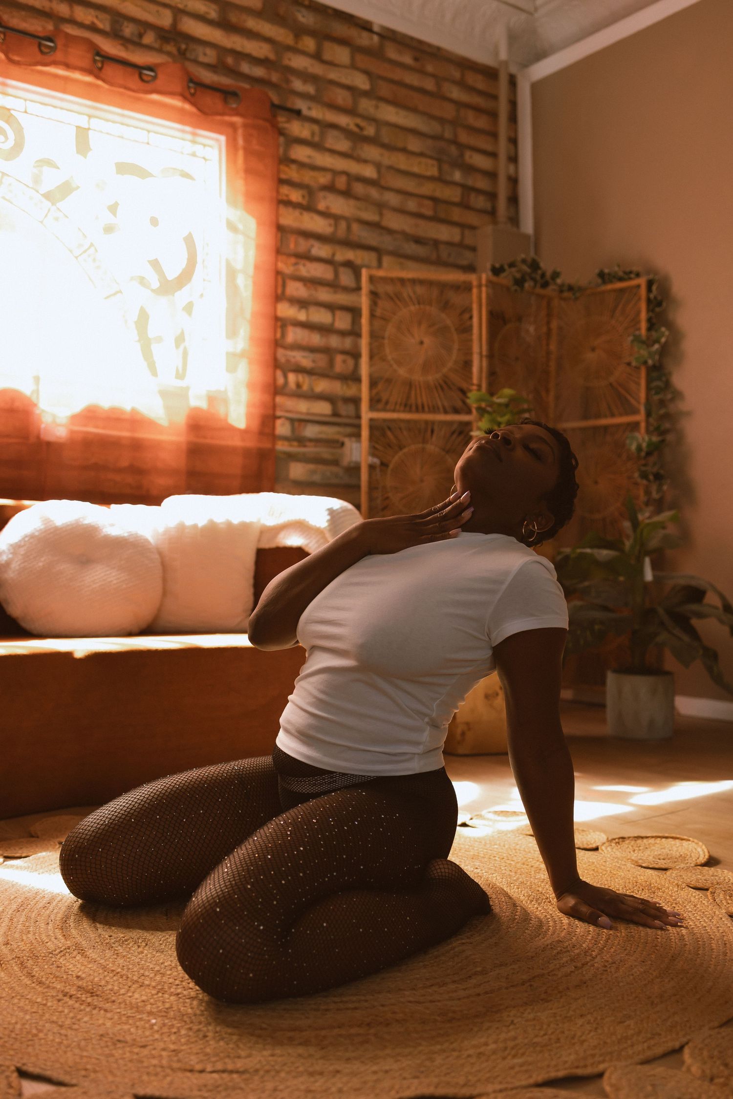 Person stretches on a round jute rug in a sunlit room with exposed brick wall and warm orange lighting.