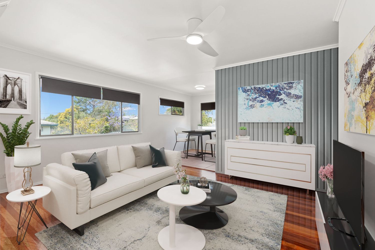 Light-filled living room with white sofa, feature wall paneling, timber floors, and open plan dining area.