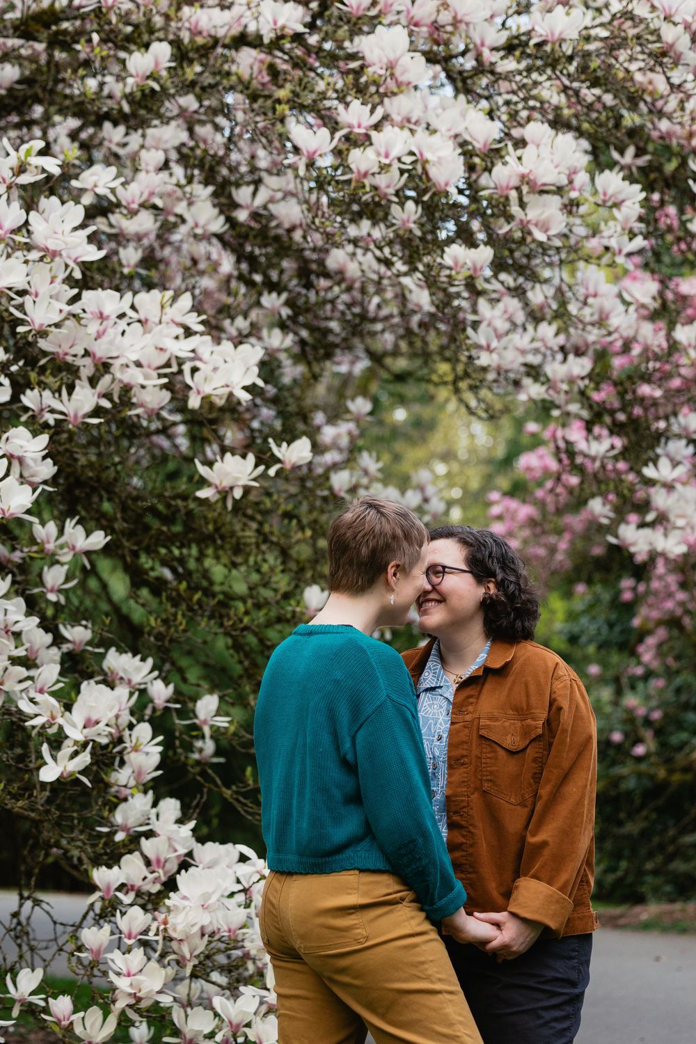 Two women about to kiss surrounded by stunning white and pink magnolia blossoms in full spring bloom.