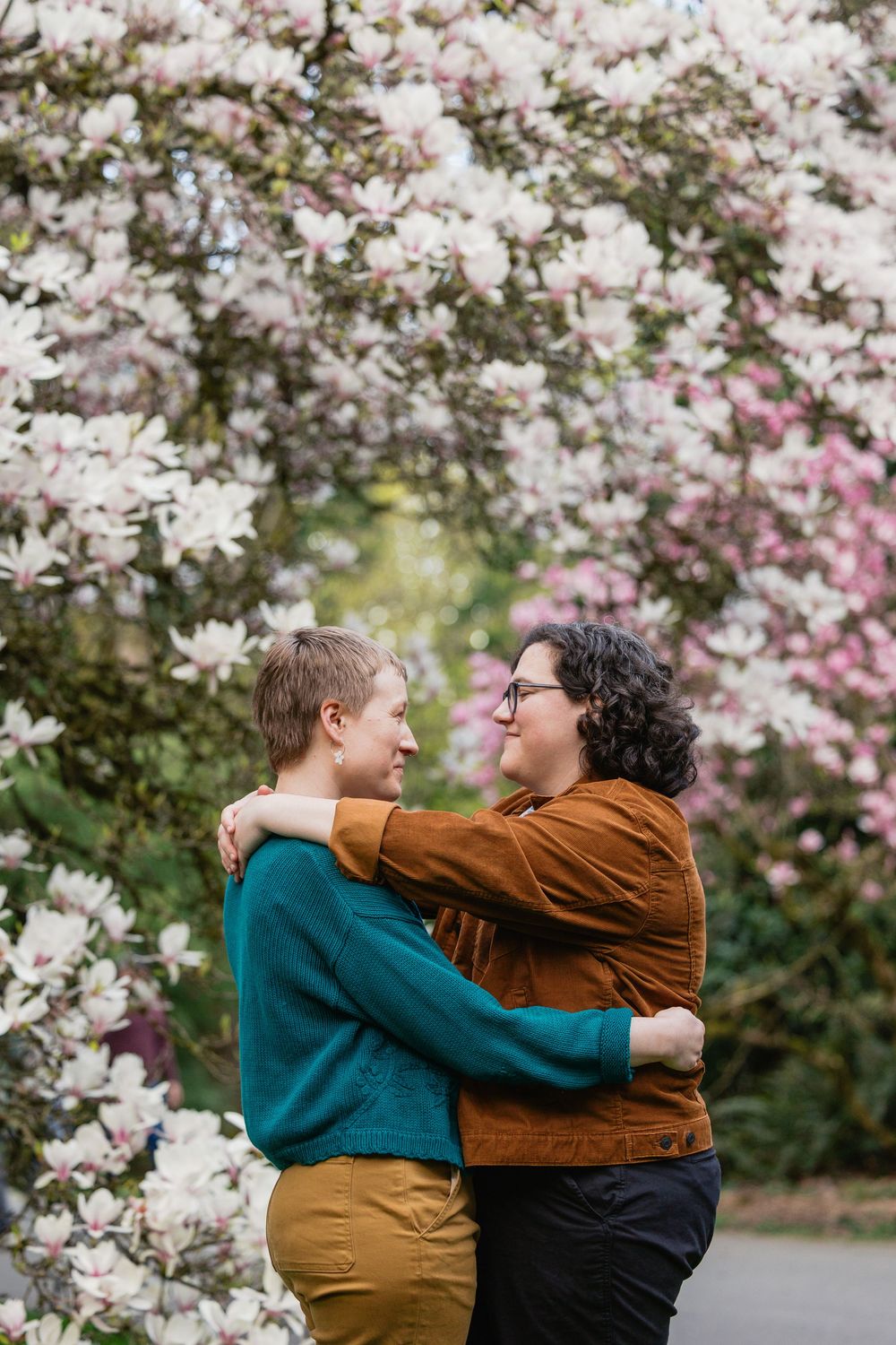 Two women embrace romantically among blooming pink magnolia trees in spring.