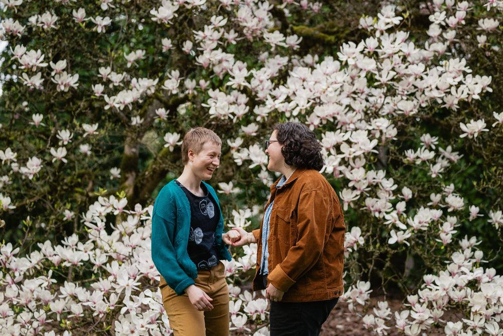 Two women smile at each other surrounded by white magnolia flowers.