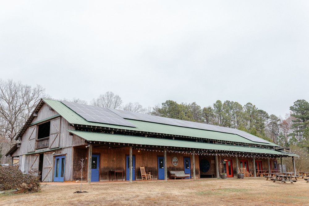 Rustic barn wedding venue with green metal roof and solar panels surrounded by winter trees.