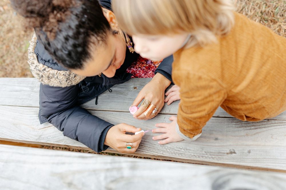 Two women closely examining rings together at weathered wooden picnic table outdoors.