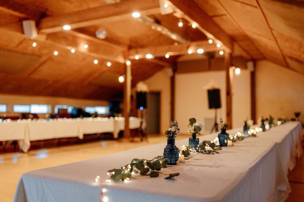 Elegantly decorated wedding reception hall with string lights and floral centerpieces on long tables.