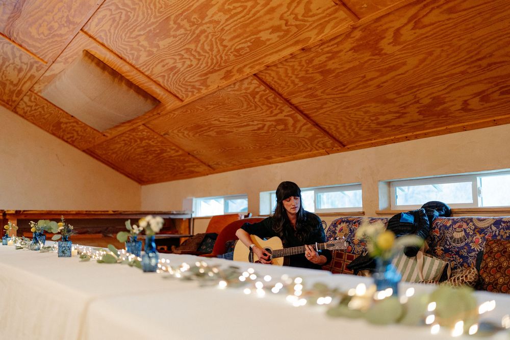 Musician plays acoustic guitar at wedding reception head table decorated with flowers and string lights.