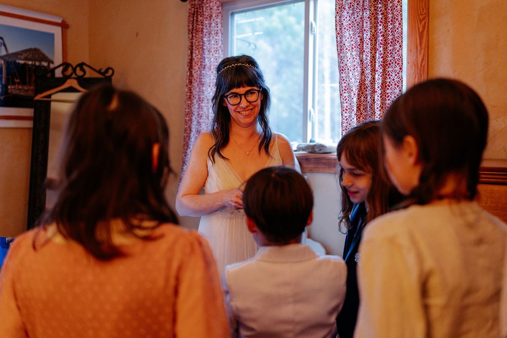 Bride in white dress interacting with children in a cozy room during wedding preparations.