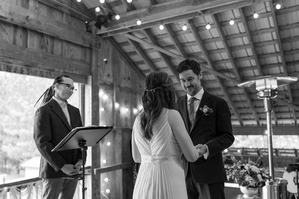 Black and white photo of a bride and groom exchanging vows at a rustic barn wedding ceremony.