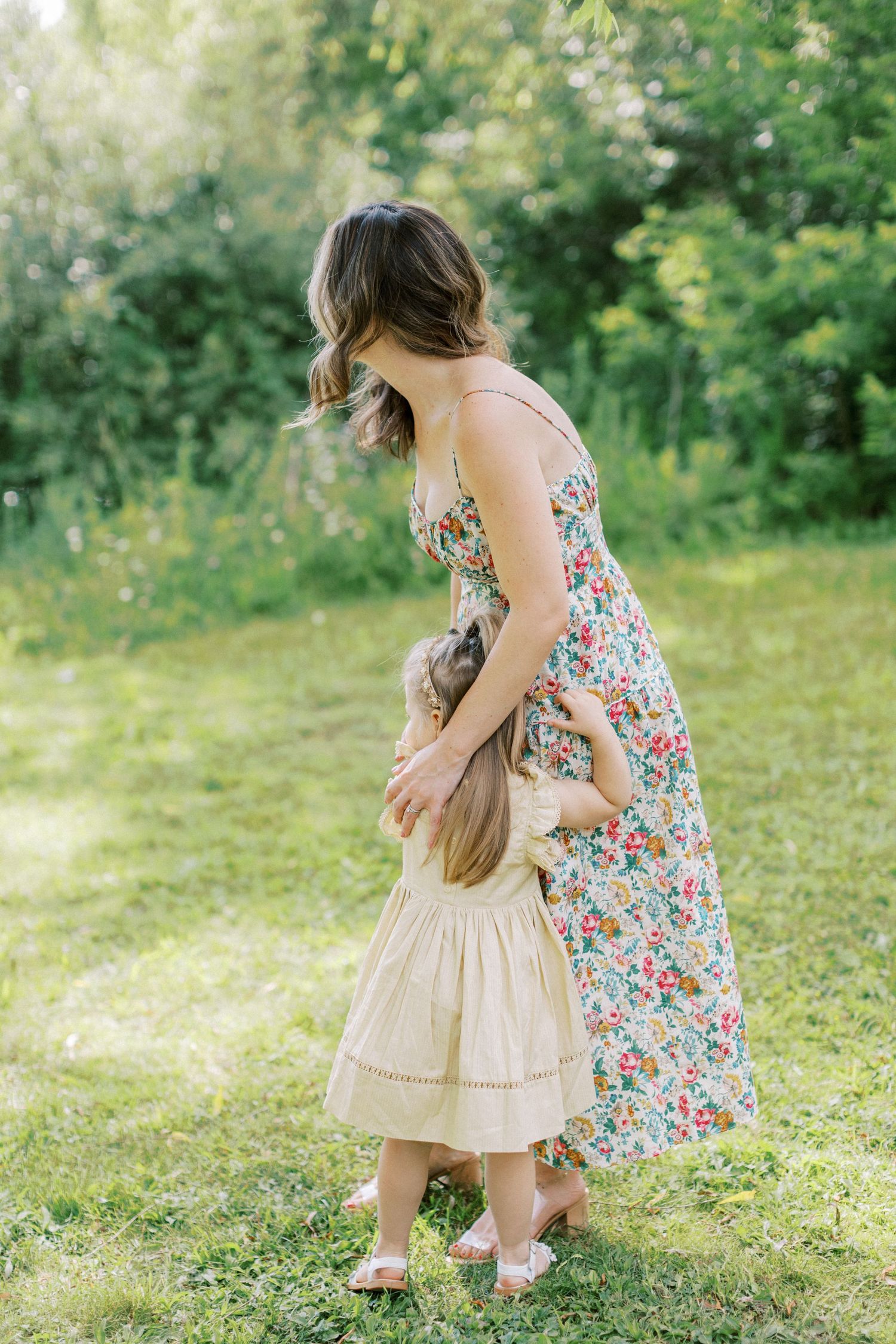 Two people in floral and beige dresses share a tender moment while dancing together in a sunny garden setting.