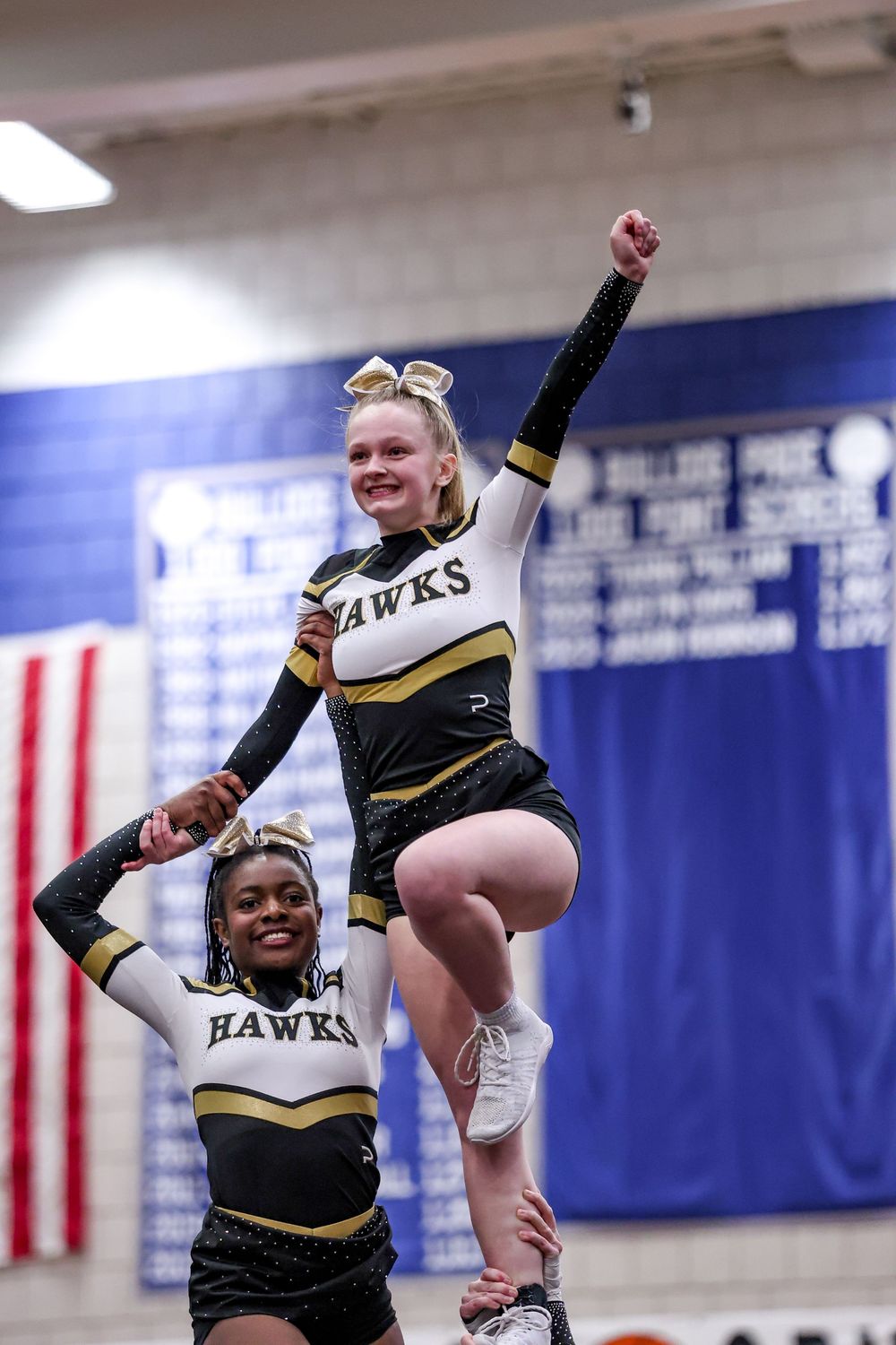 Two cheerleaders from the Hawks team perform a partner stunt during a competition routine.