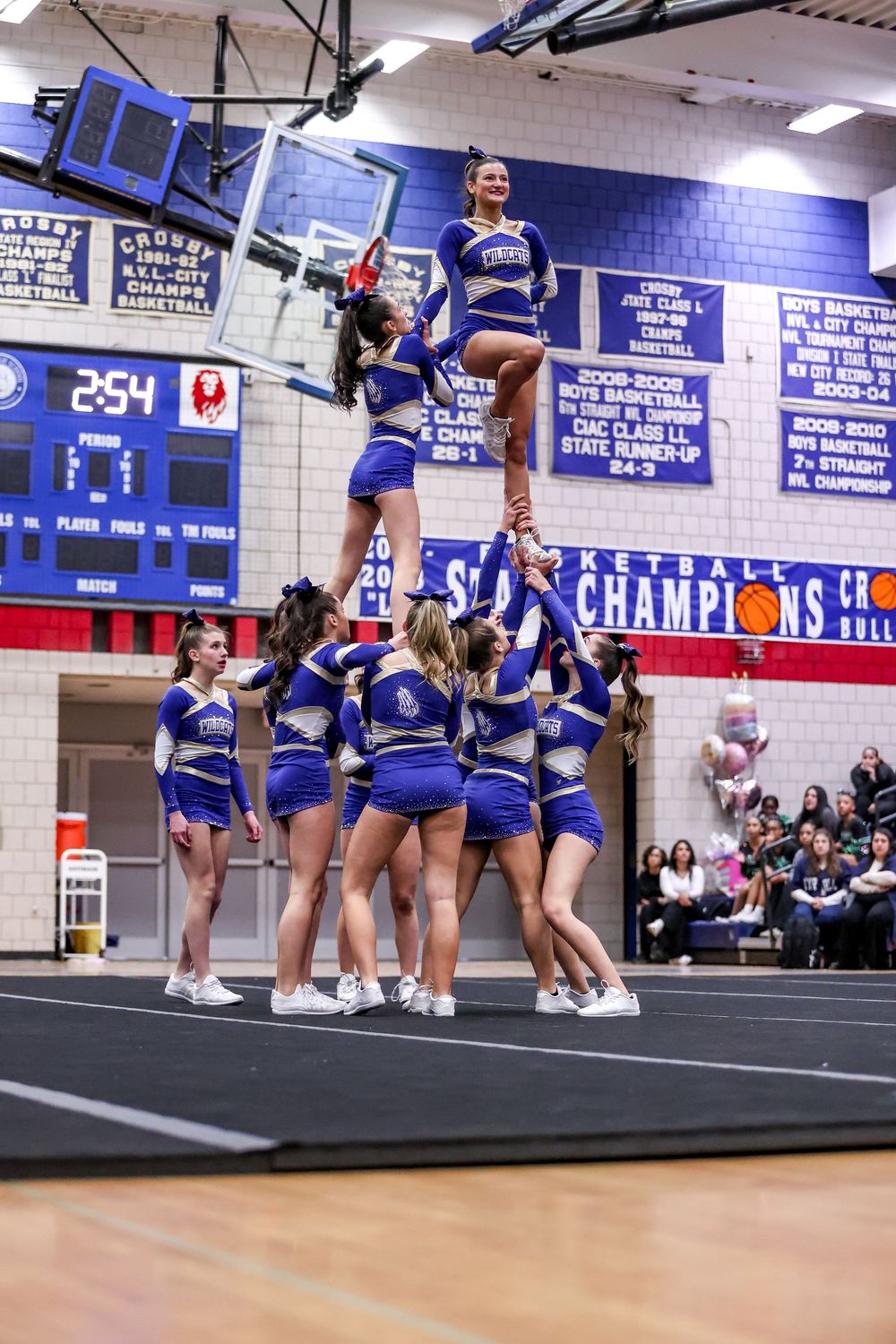 Cheerleaders execute a complex pyramid formation in blue uniforms during an indoor competition performance.