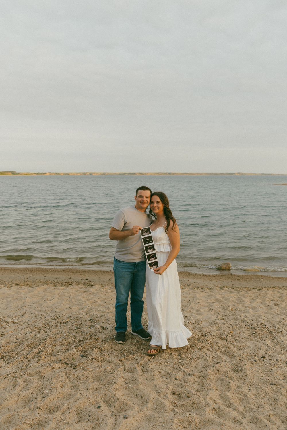 A couple shares a romantic moment together on a sandy beach at sunset with the ocean in the background.
