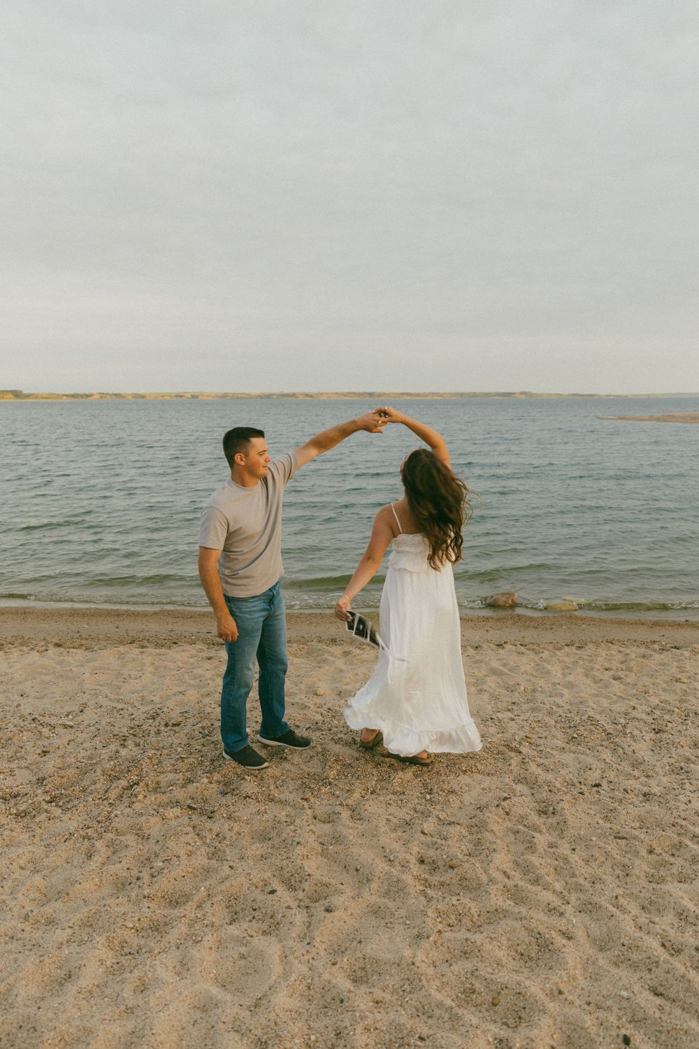 A couple dancing together on a sandy beach at sunset with calm waters in the background.