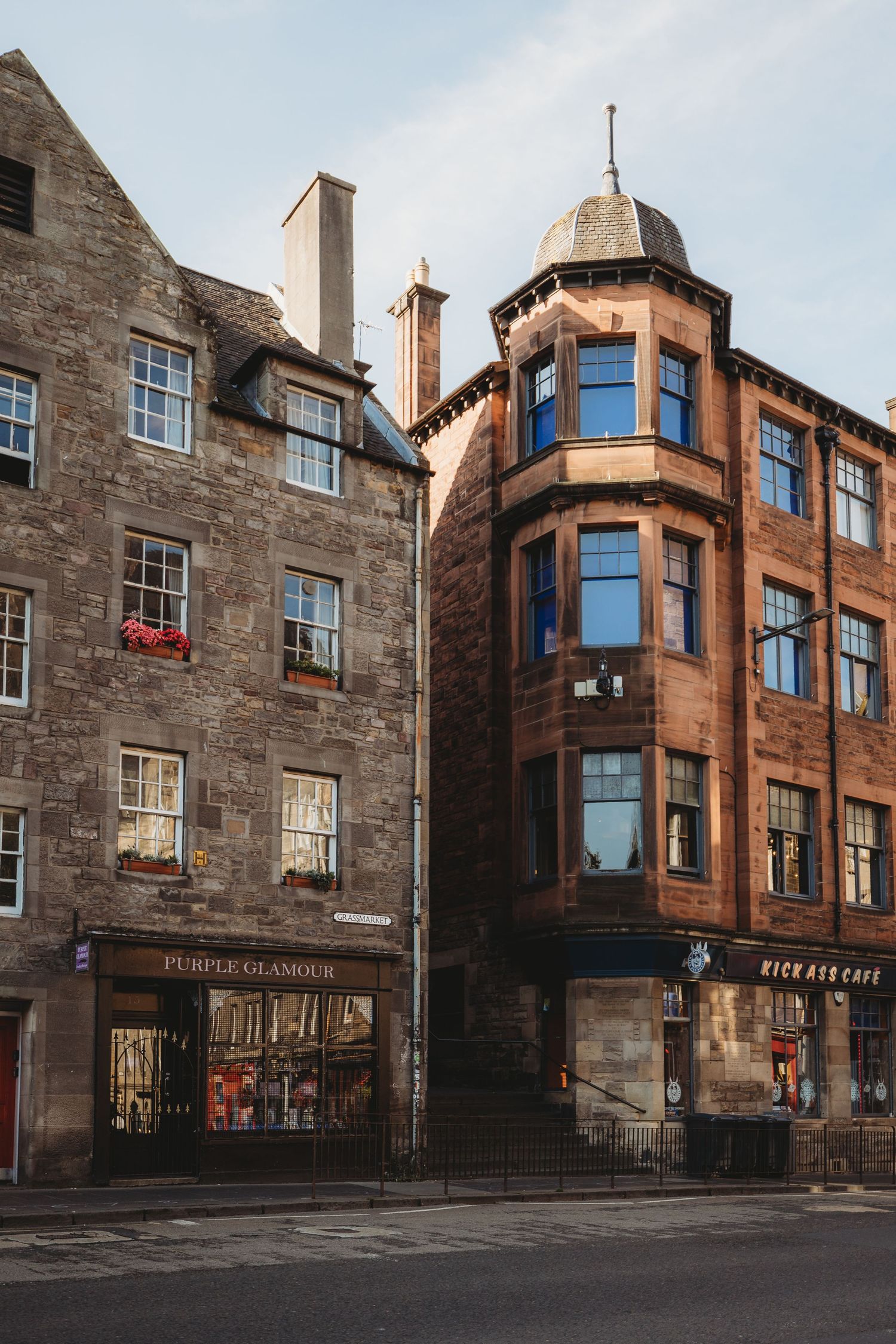 Historic stone buildings with bay windows and storefronts line a quaint street corner in Edinburgh's Old Town.