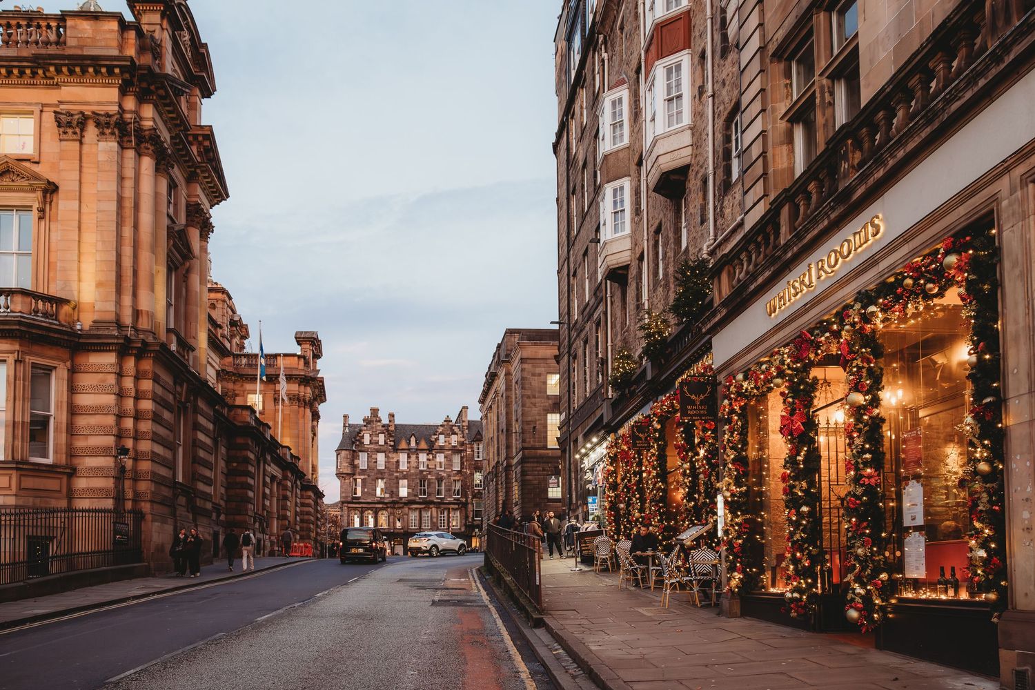 Historic Edinburgh street with stone buildings and holiday decorations glowing at dusk along Victoria Street.