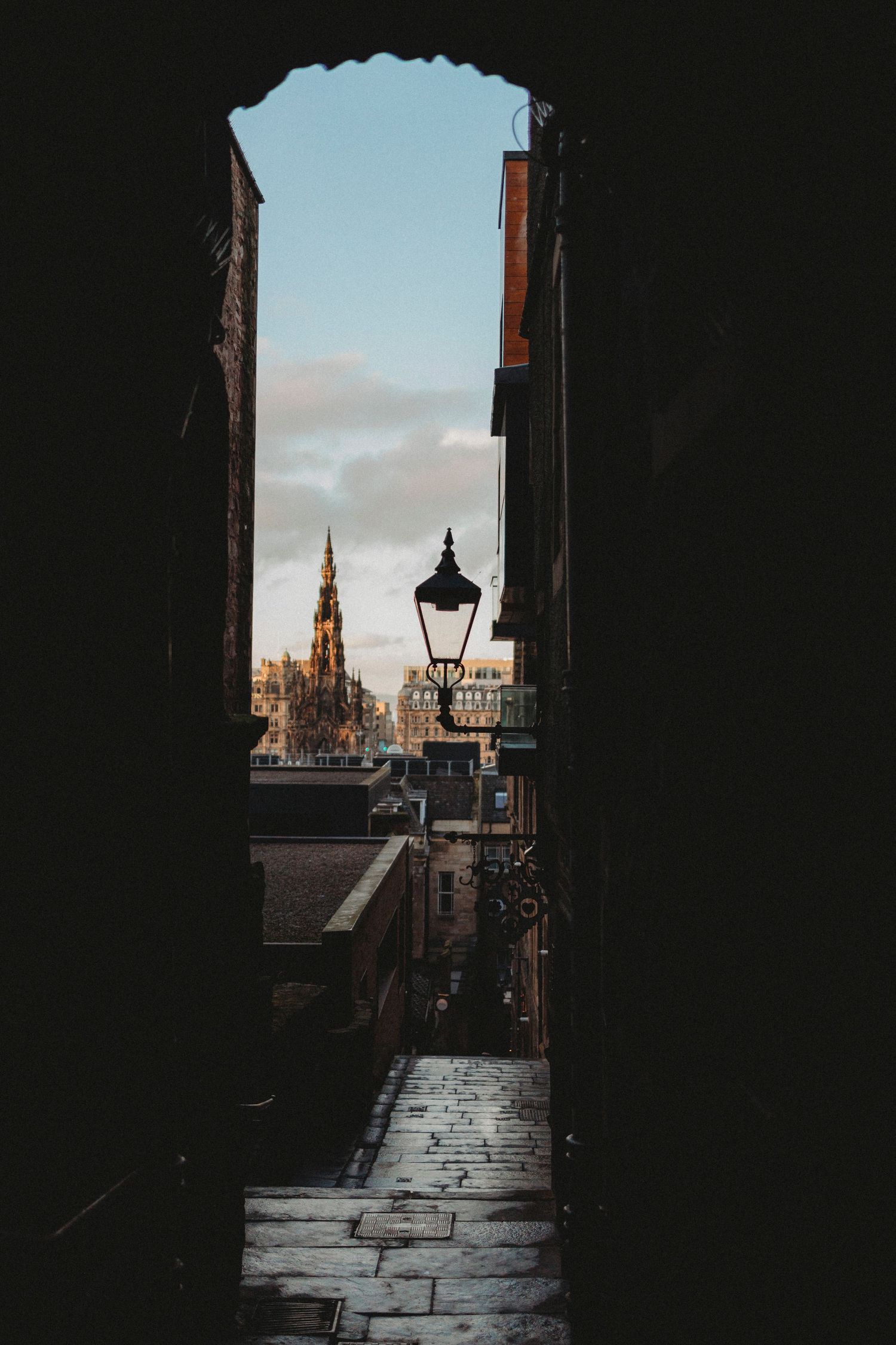 A dark alleyway in Edinburgh reveals historic architecture and church spires silhouetted against a moody sky.