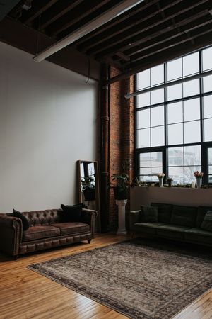 Modern industrial loft space with exposed brick walls, large windows, hardwood floors, leather sofa and decorative area rug.