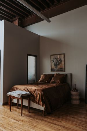 Spacious bedroom with hardwood floors, exposed wooden beams, and brown bedding in a modern minimalist design.