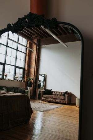 Industrial loft space with exposed brick walls, large windows, hardwood floors and brown leather Chesterfield sofa.