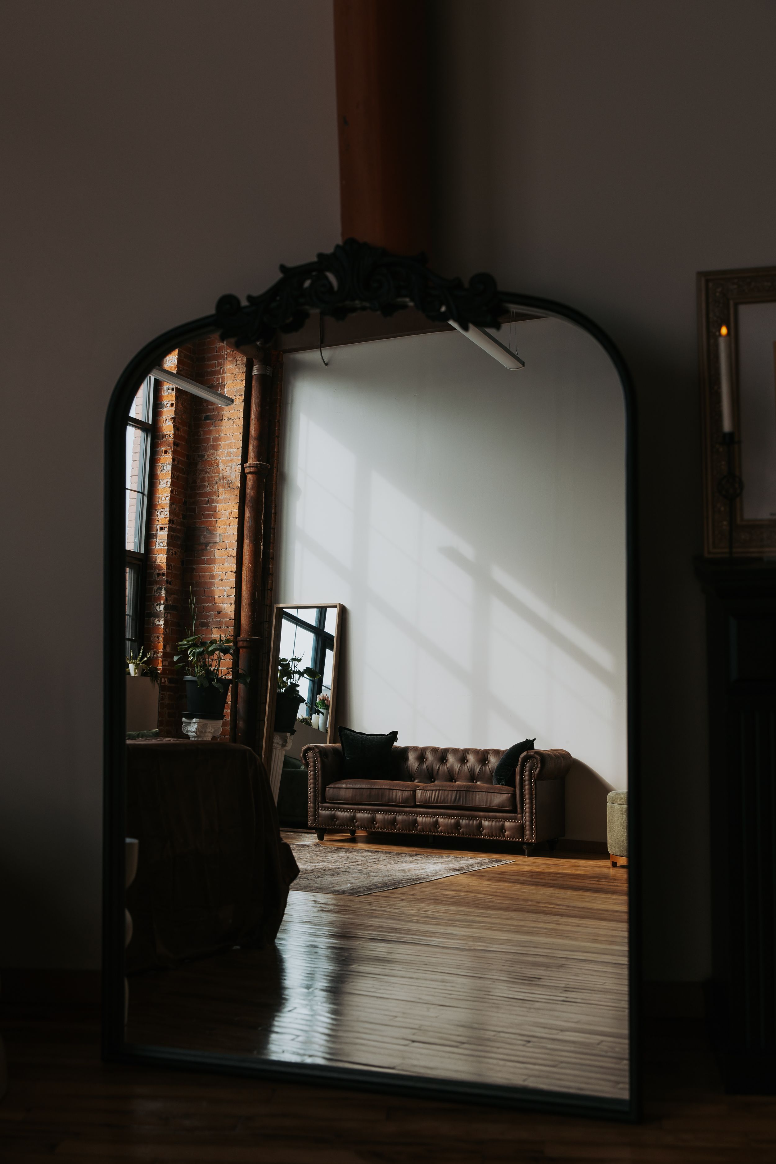 Sunlight streams through windows onto hardwood floors in a dark, minimalist room with exposed brick walls.