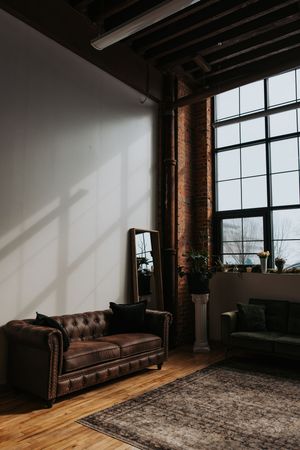 Industrial loft interior with leather chesterfield sofa, hardwood floors, exposed brick walls and large windows.