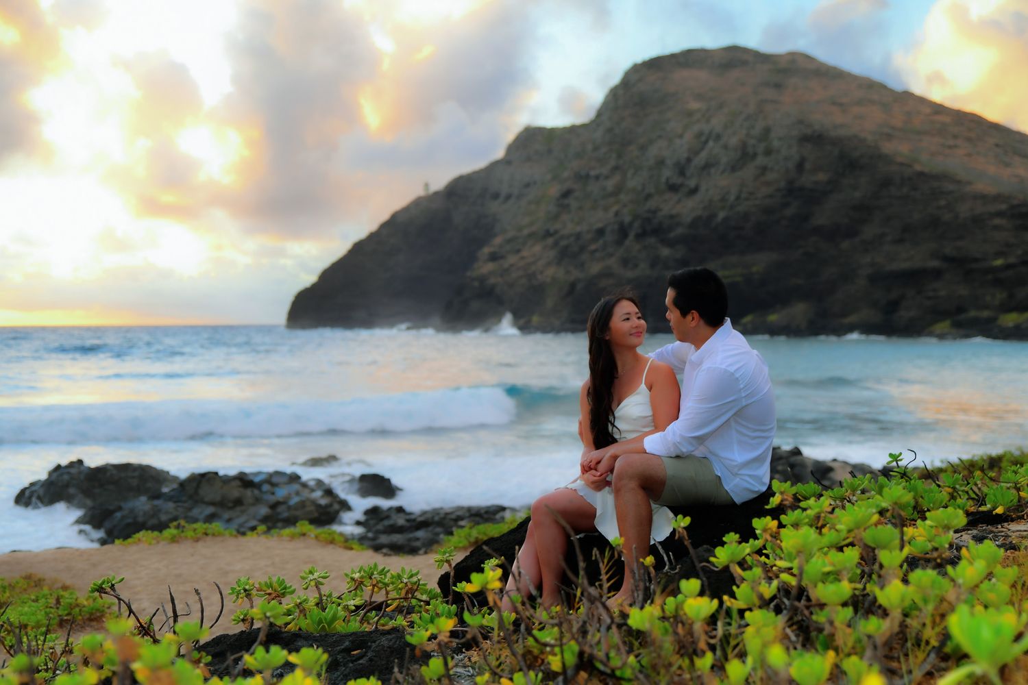 A couple shares a romantic moment at sunset on a scenic coastal cliff overlooking the ocean in Hawaii.