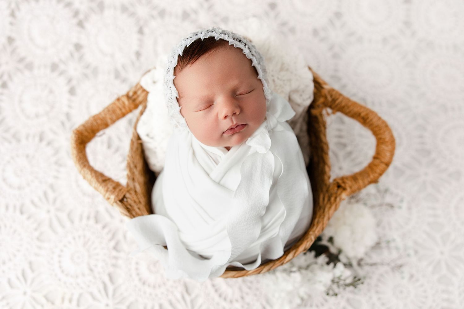 Sleeping newborn baby wearing white outfit lies on soft white blanket surrounded by decorative cookie pieces.