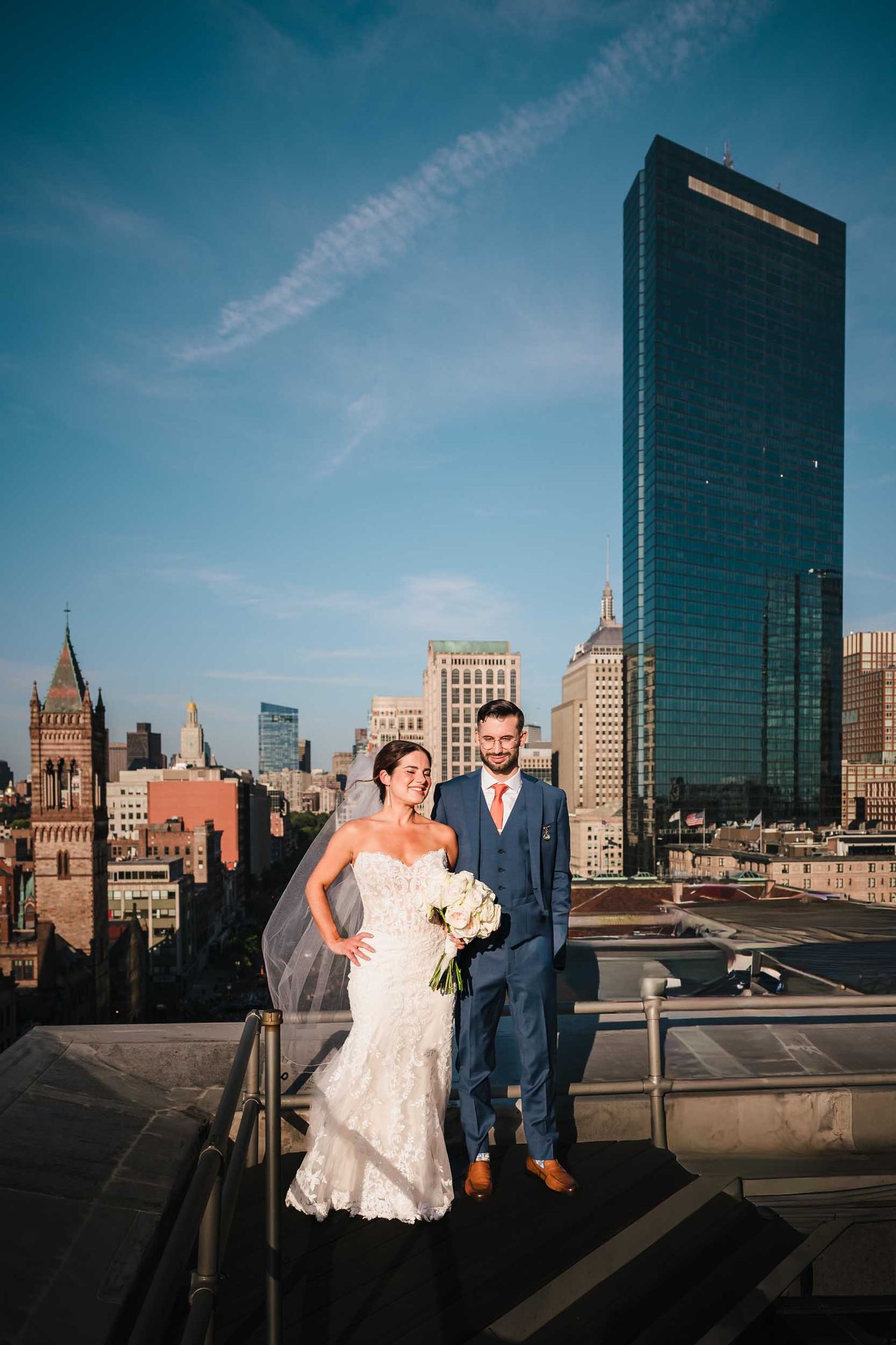 Bride and groom posing on the Lenox Hotel rooftop with the Boston skyline and John Hancock Tower in the background