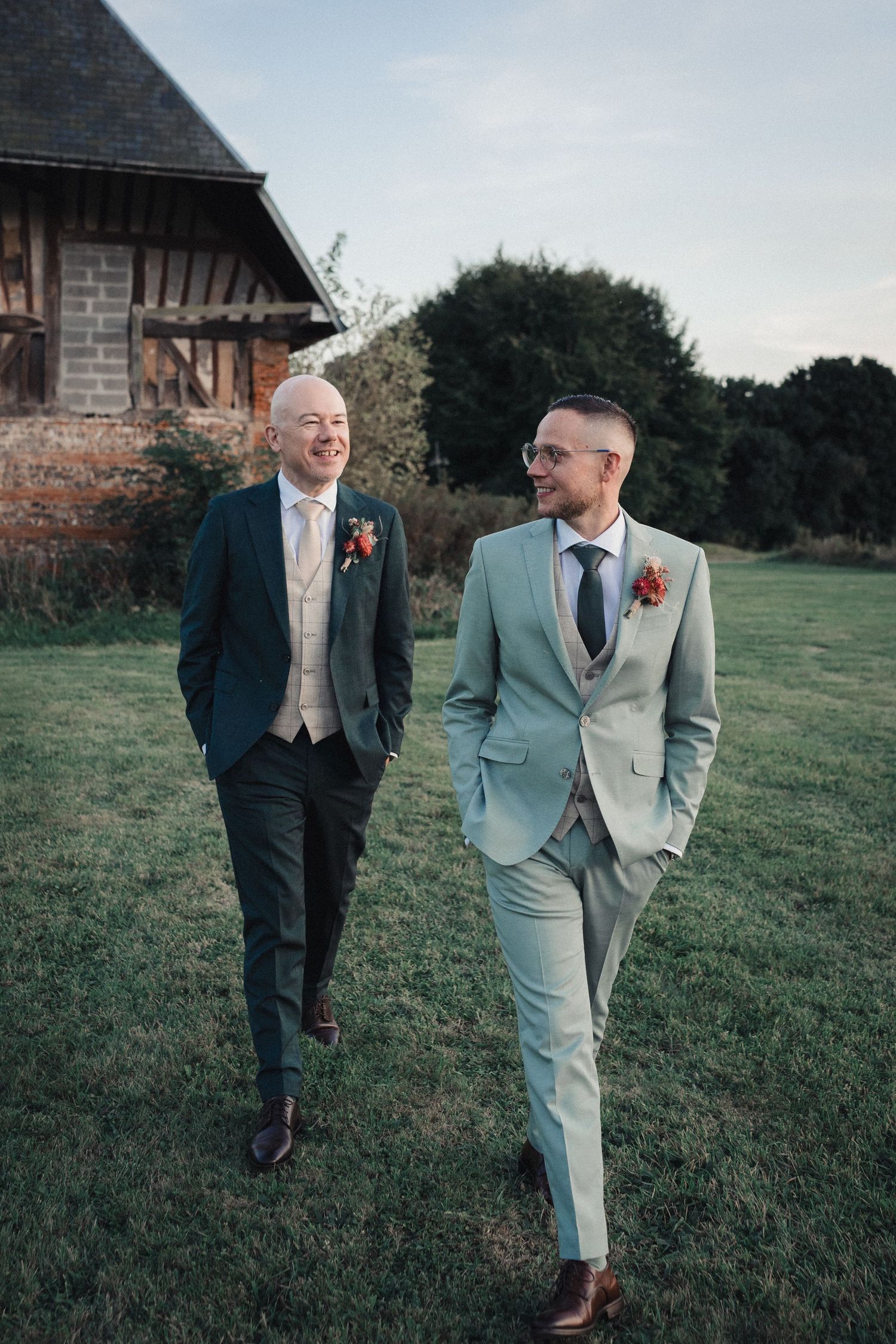 Two men in contrasting suits having a conversation while standing in a grassy field with trees in the background.