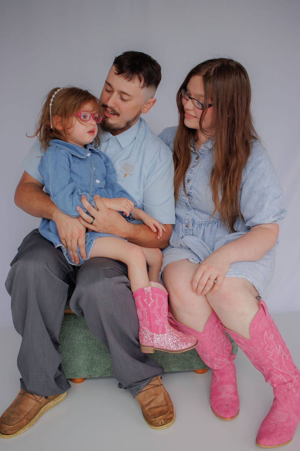 A family of four, including a man, woman, and two young girls, sitting together on a couch and smiling.