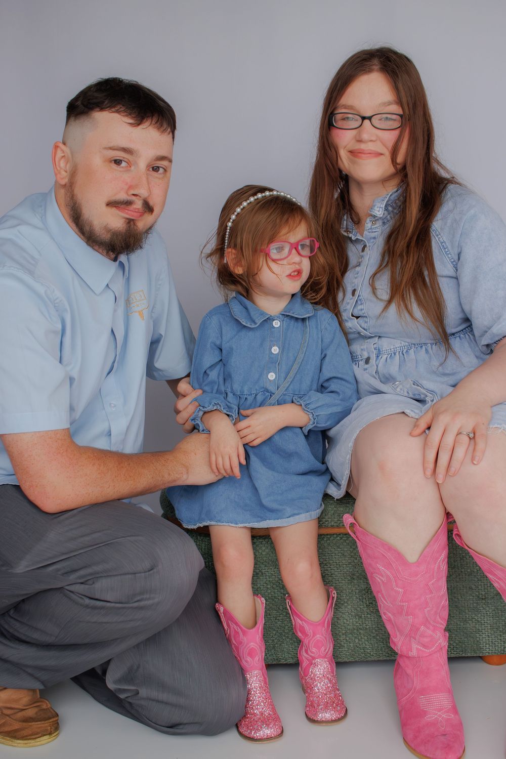 Family portrait featuring coordinating denim outfits and pink boots against grey background.