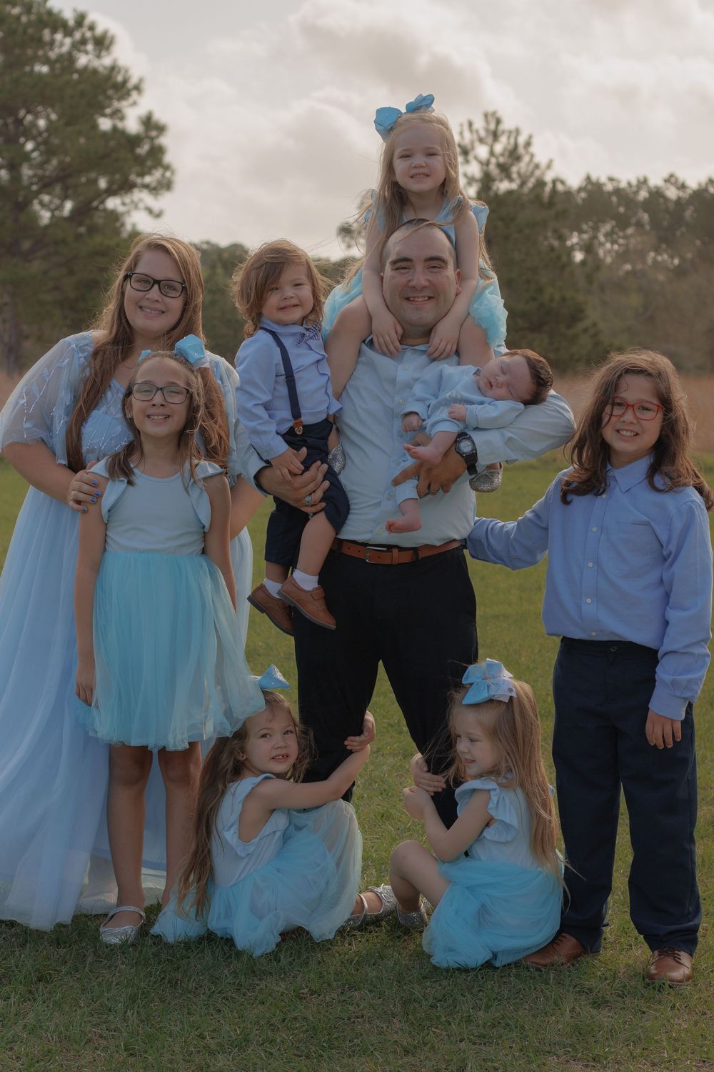 A large family in matching blue outfits poses together outdoors on a grassy field.