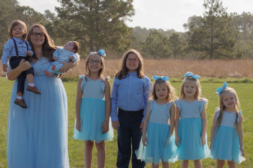 A large family, including several children, stands together in a grassy field with trees in the background.
