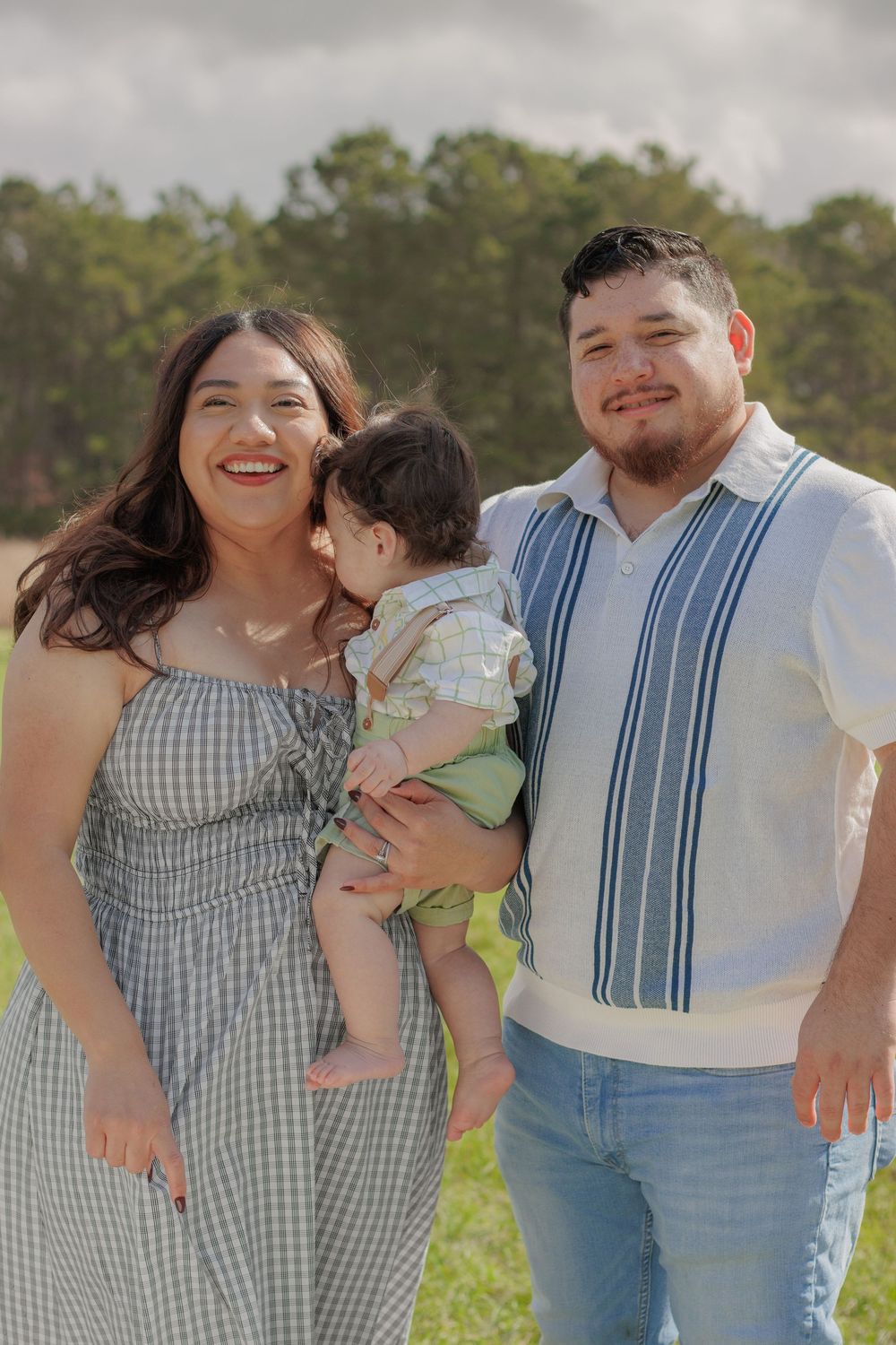A happy family of three, including a woman, a man, and a young child, standing together in a grassy field.