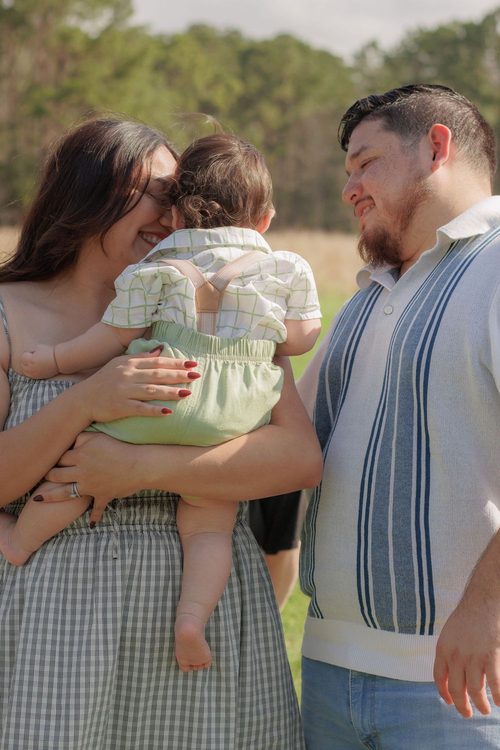 A family of three, a mother, father, and young child, standing together outdoors in a natural setting.