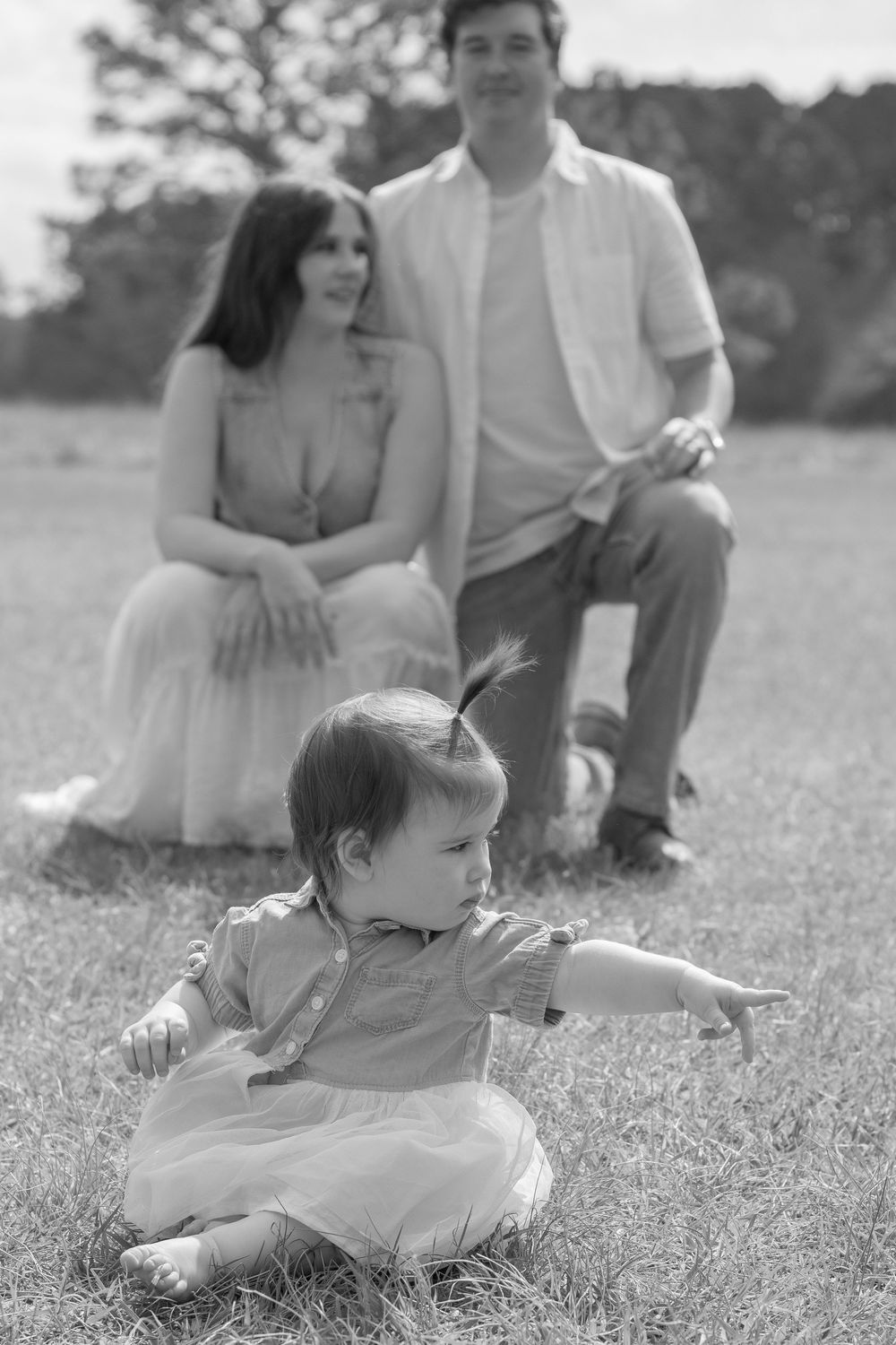 A black and white image shows a couple sitting on the grass, with a young child playing in the foreground.