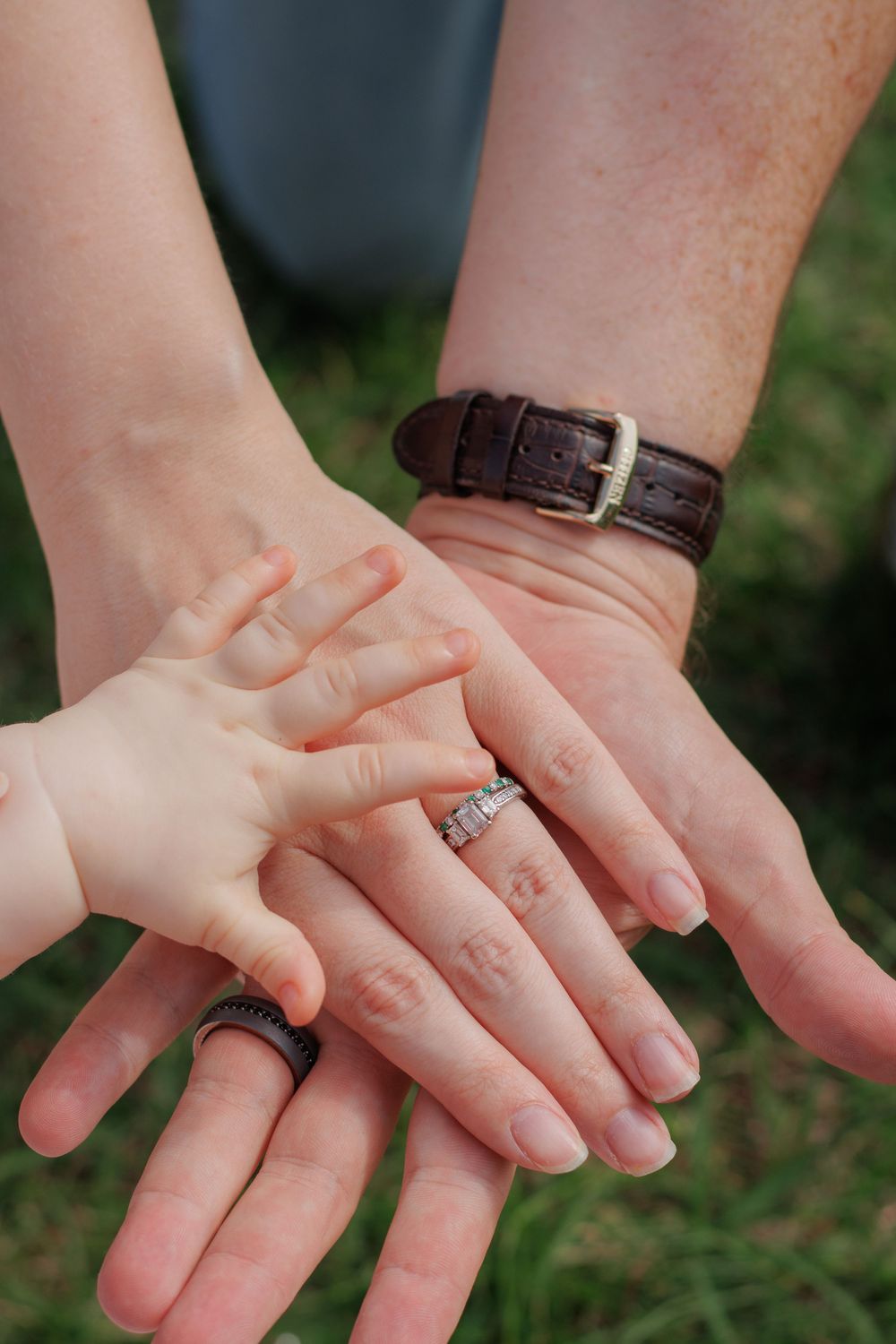 The image shows two hands clasped together, with one person wearing a leather bracelet and the other wearing a ring.